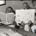 Alunos numa sala de aula da Praia mostram livros ao fotógrafo, numa imagem de arquivo da UNESCO sem data indicada na página original. A fotografia ilustra a leitura e não documenta o concurso de 2026.